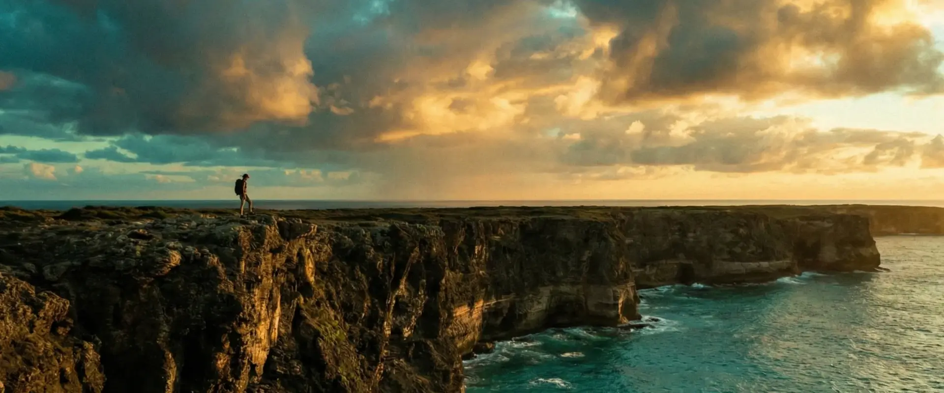 Coastal cliff overlooking turquoise ocean at sunset